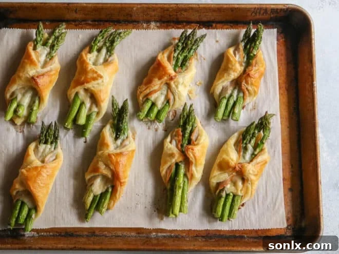 Close up view of uncooked asparagus and pancetta bundles on puff pastry before baking.