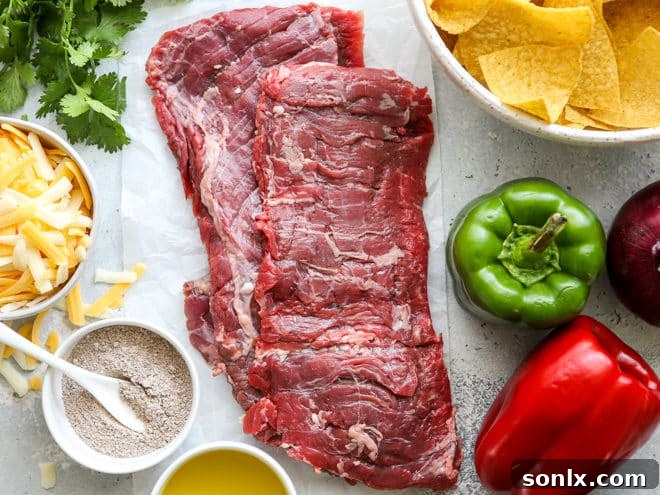 A vibrant selection of fresh ingredients including marinated skirt steak, sliced bell peppers, red onion, and cilantro, ready for steak fajita nachos.