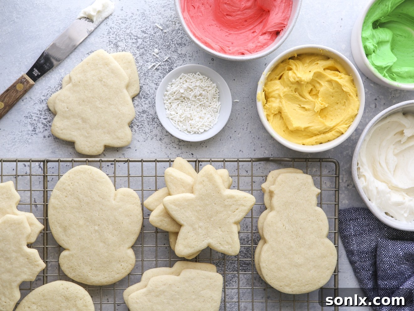A collection of freshly baked sugar cookies ready for decoration, alongside bowls of vibrant frosting and an assortment of colorful sprinkles.