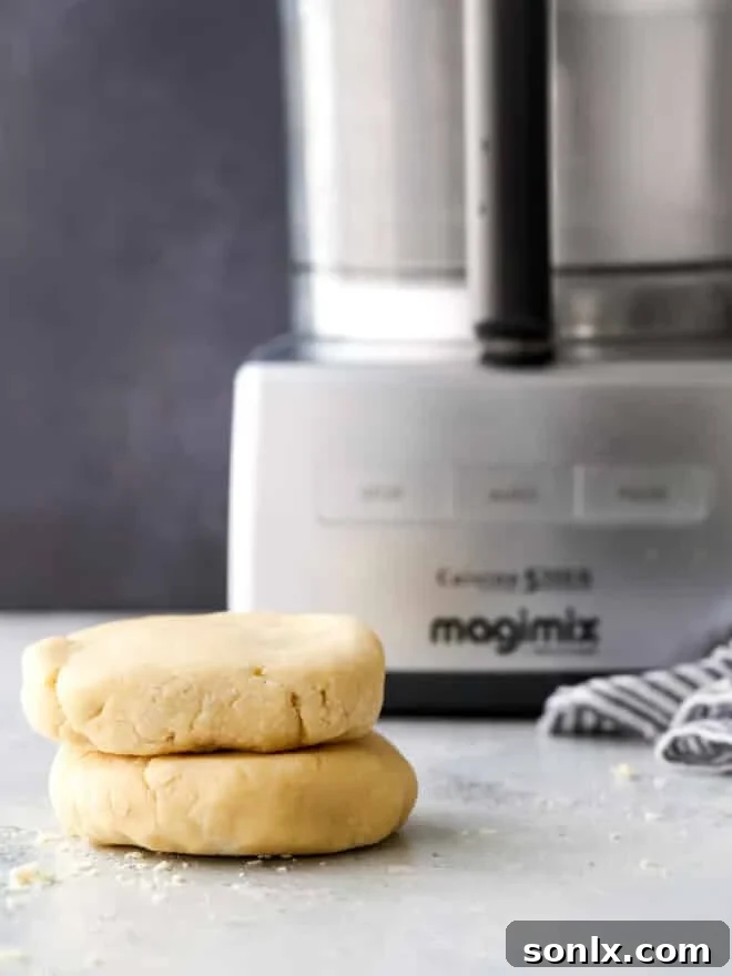Stack of pie crust disks next to a food processor, highlighting the ease of preparation.