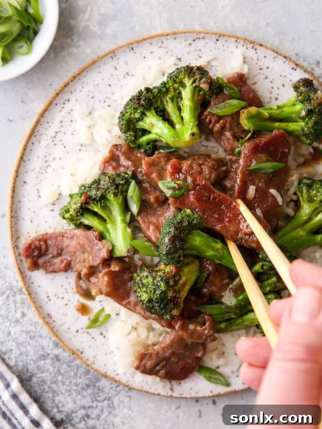 A close-up of Beef and Broccoli Stir Fry, garnished with green onions, with chopsticks resting on the side, inviting a taste.