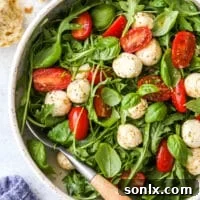 Closeup of Arugula Caprese Salad in a bowl, showing the vibrant colors of tomatoes, mozzarella, and greens.