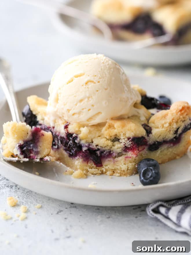 blueberry pie bars with a scoop of ice cream on a plate, bite taken out