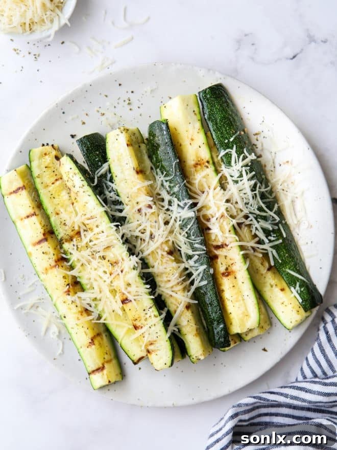 close up of perfectly grilled parmesan zucchini on a plate, garnished with fresh herbs