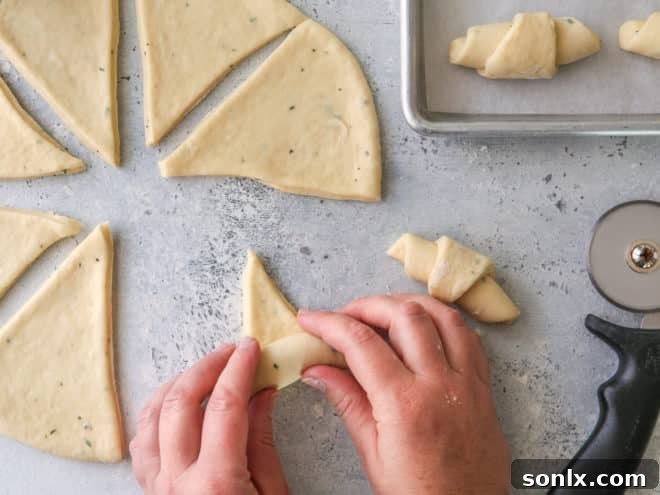 A person rolling up herb dinner crescent rolls from a triangular dough piece