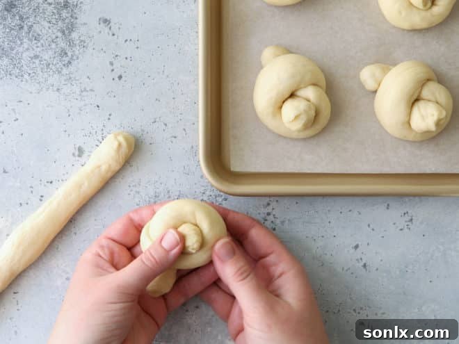 A person shaping white dinner roll knots from dough ropes