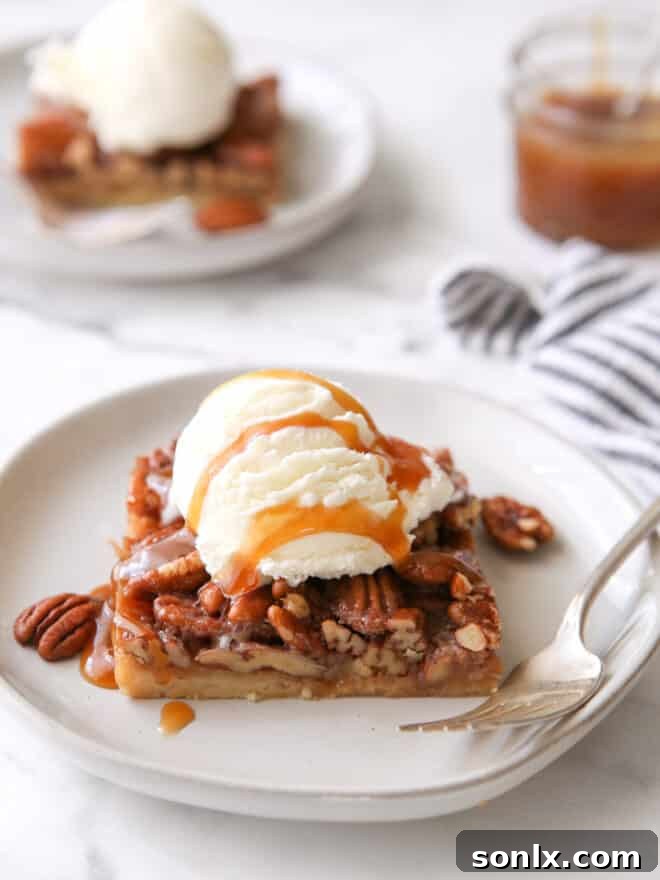 Gooey Pecan Pie Bar topped with melting vanilla ice cream and a swirl of caramel sauce on a white plate