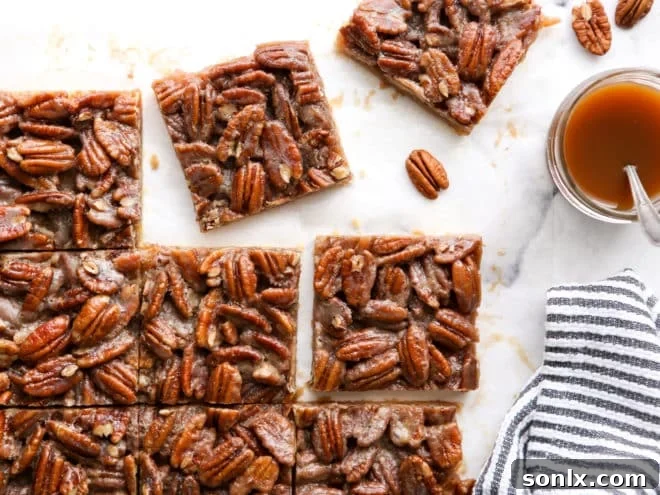 Neatly cut pecan pie bars arranged on a plate, with a jar of rich caramel sauce in the background
