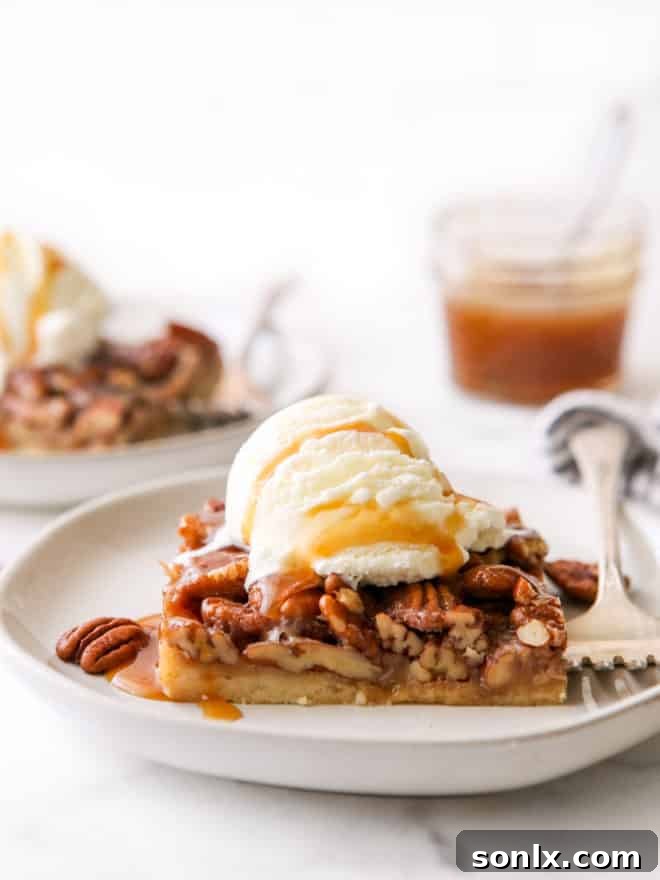 Close-up of a single pecan pie bar on a plate, adorned with a scoop of vanilla ice cream and a generous caramel drizzle