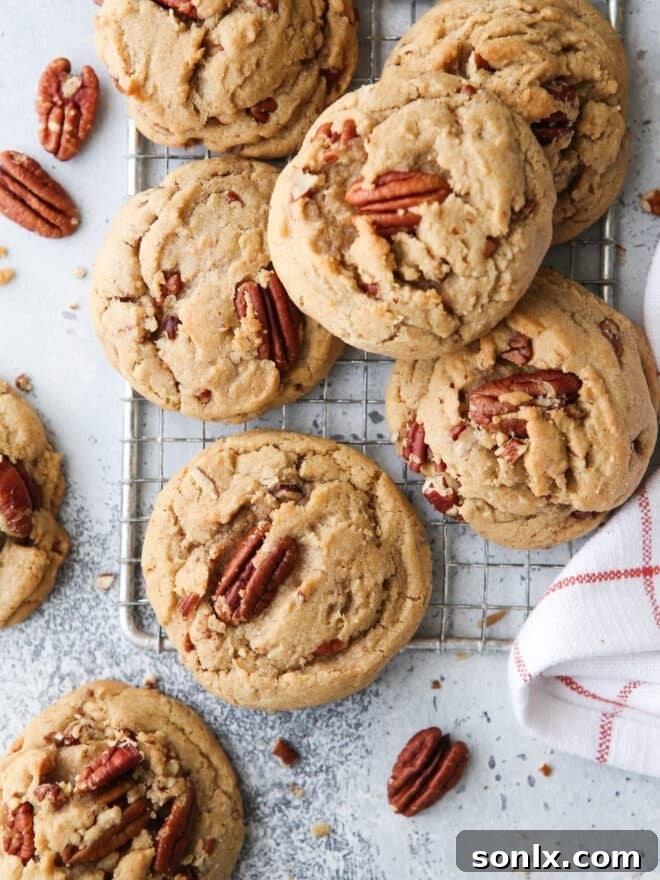 Closeup of golden brown butter pecan cookies on a wire cooling rack, showing their chewy texture and embedded pecan pieces.
