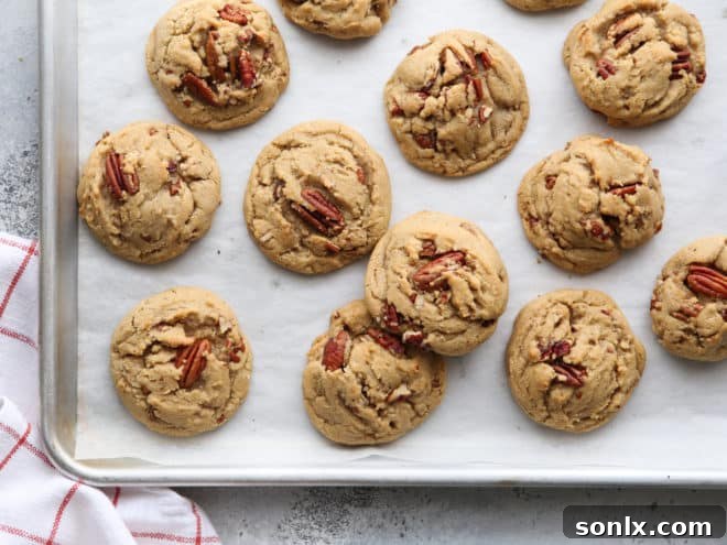Warm, freshly baked brown butter pecan cookies cooling on a parchment-lined baking sheet, their golden edges visible.