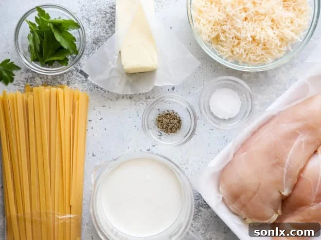 All the ingredients for chicken fettuccine alfredo laid out on a table: chicken, pasta, butter, cream, parmesan cheese, salt, and pepper.