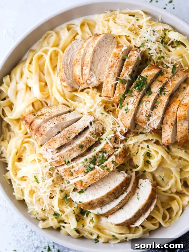 A close-up shot of creamy chicken fettuccine alfredo in a white bowl, garnished with parsley.