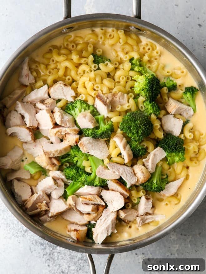 A large spoon stirring chicken broccoli macaroni and cheese in a black skillet