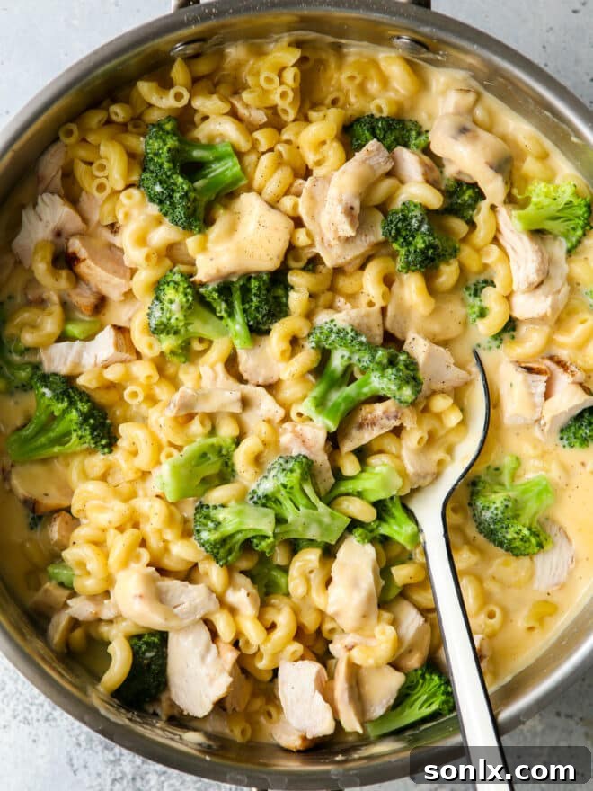 Close-up of chicken broccoli macaroni and cheese being stirred with a large serving spoon in a skillet