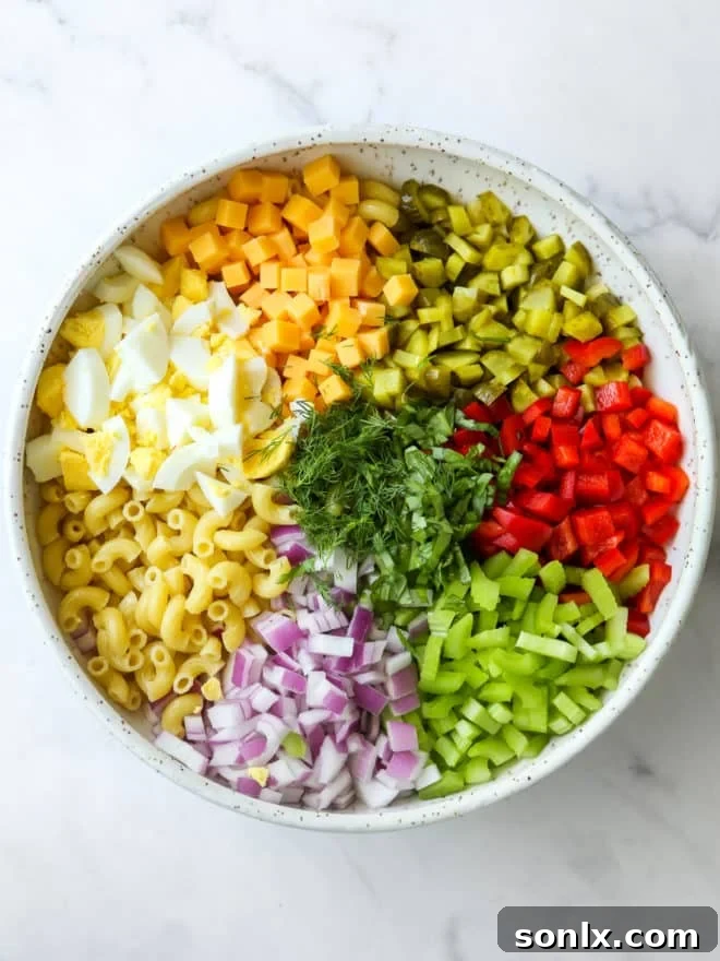 A large mixing bowl filled with all the ingredients for macaroni salad, including cooked pasta, diced vegetables, cheese, and eggs, before the dressing is added.