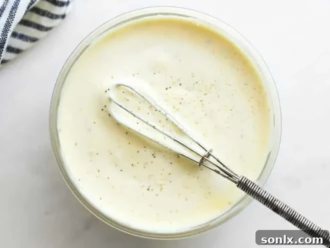 Close-up shot of a whisk combining the creamy ingredients for the macaroni salad dressing in a glass bowl.
