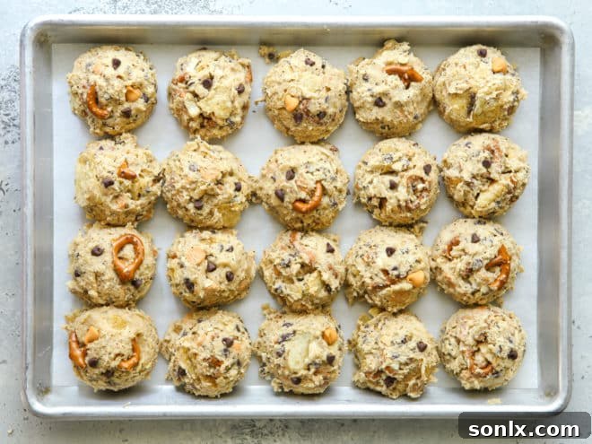 Scooped, unbaked kitchen sink cookie dough balls arranged on a parchment-lined sheet pan