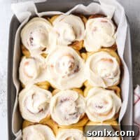 A delicious Eggnog Cinnamon Roll on a white plate, showcasing its golden-brown crust and creamy icing.