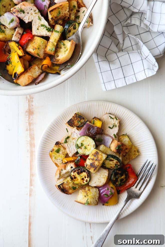 A large serving bowl filled with the complete grilled chicken and vegetable panzanella salad, garnished with fresh herbs.