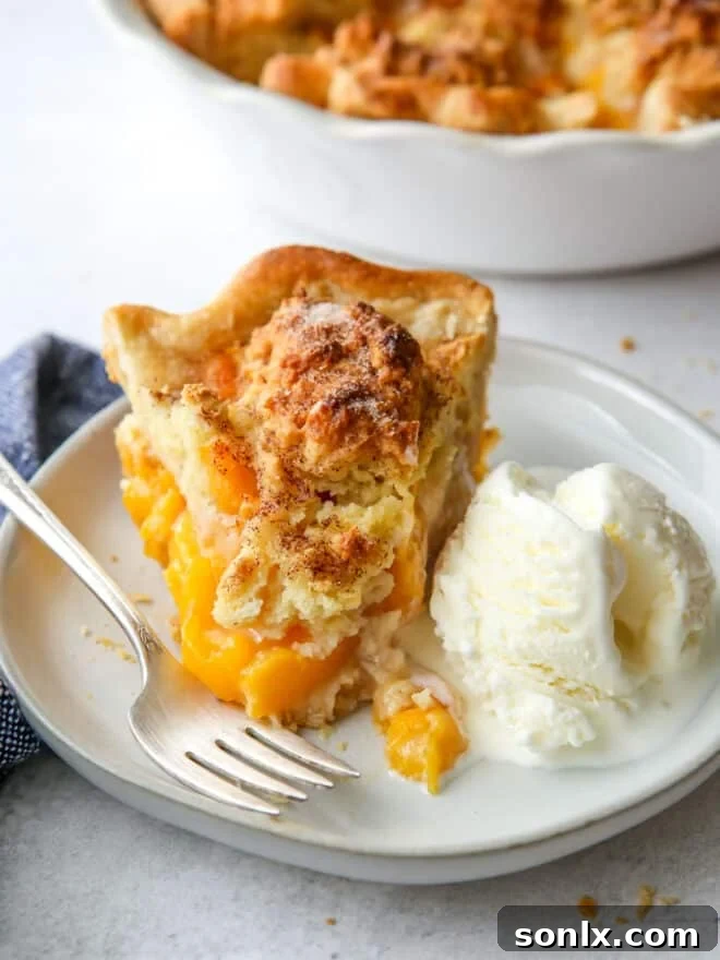 A slice of peach cobbler pie with a dollop of vanilla ice cream, ready to be enjoyed.