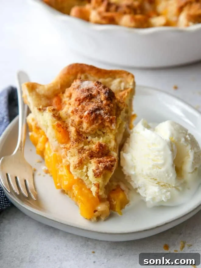 A slice of warm peach cobbler pie on a plate, topped with a generous scoop of melting vanilla ice cream.
