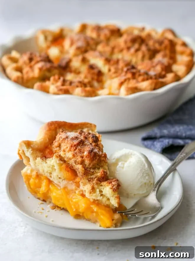 A close-up view of a slice of peach cobbler pie on a white plate, highlighting the textures of the filling and topping.