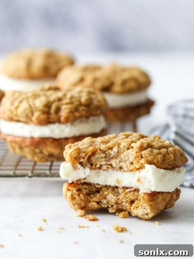 A perfectly assembled oatmeal cream pie cookie with a bite taken out, revealing the creamy marshmallow filling between two chewy oatmeal cookies.