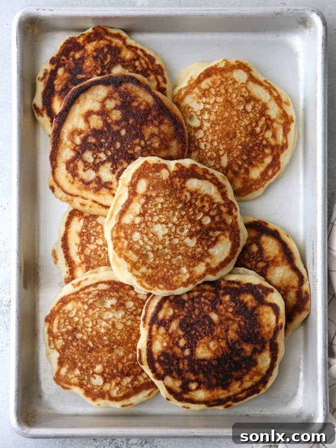 A close-up of a skillet cooking golden-brown buttermilk pancakes, with bubbles forming on the uncooked side, indicating readiness for flipping.