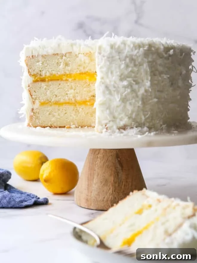 A beautifully sliced lemon coconut cake on an elegant cake stand, revealing its moist layers, bright lemon curd, and fluffy white frosting.