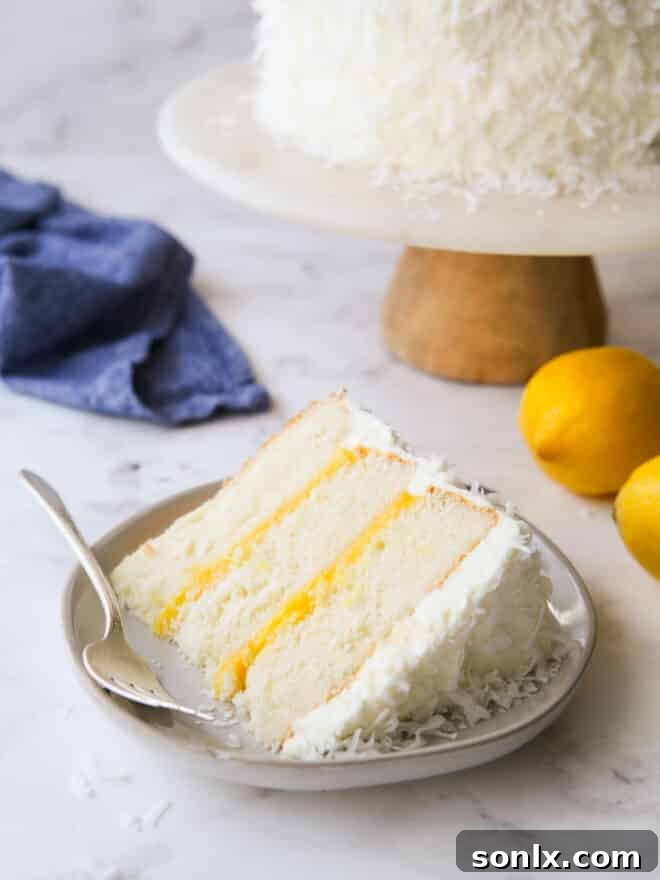 A beautifully presented slice of lemon coconut cake on a white plate, showcasing the layers of cake, curd, and frosting.