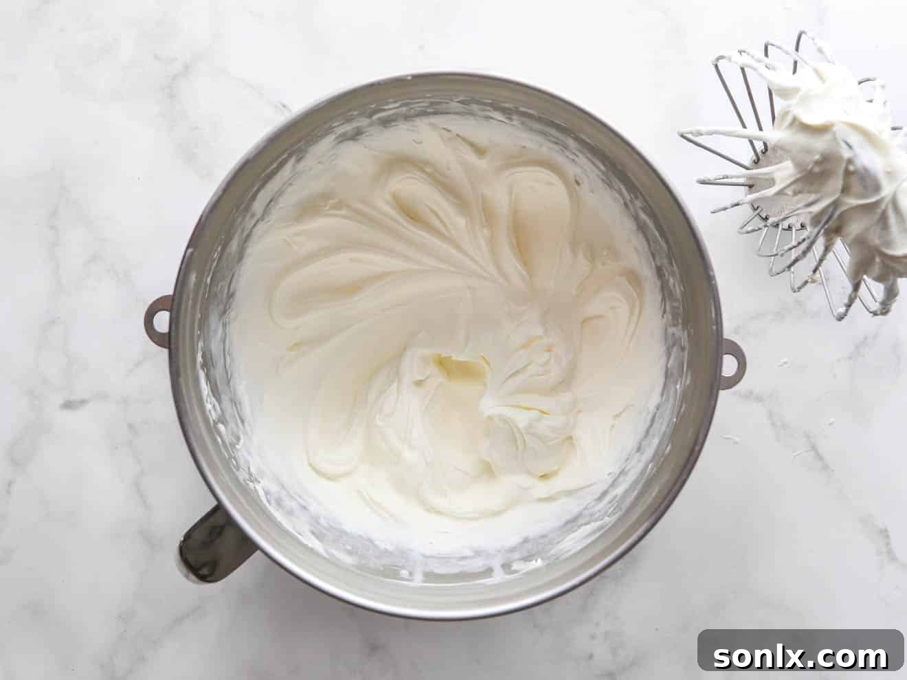 A mixing bowl filled with perfectly whipped Chantilly cream frosting, showing its fluffy, ethereal texture.