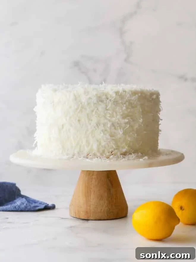 The fully assembled lemon coconut cake, beautifully frosted and decorated with shredded coconut, resting on a white cake stand.