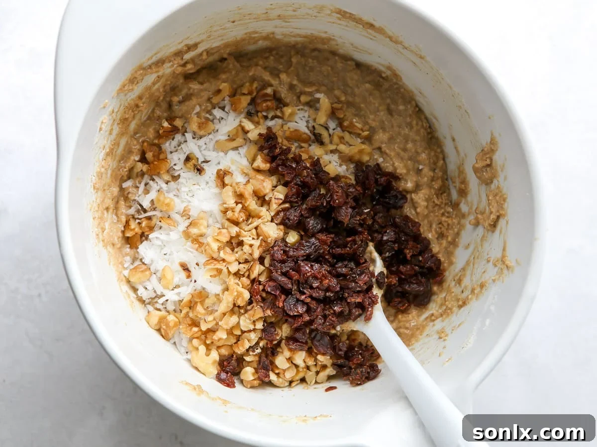 Close-up shot of hands gently mixing bran muffin batter in a white bowl with a spatula, showing the initial combination of wet and dry ingredients.