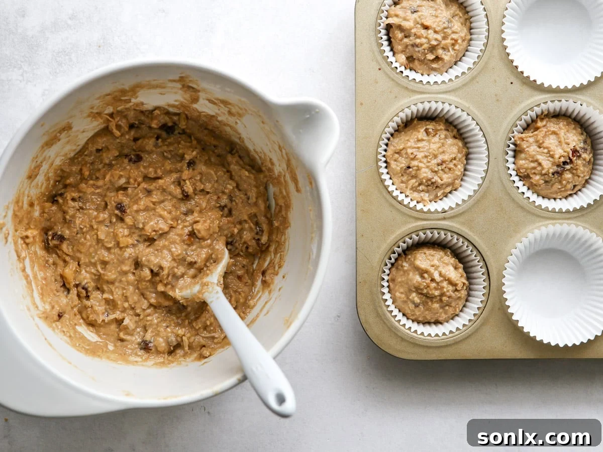 A close-up of muffin batter being scooped into a muffin pan lined with paper liners, ready for baking.