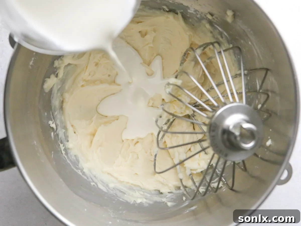 Pouring heavy cream into the mixing bowl with the cream cheese mixture, gradually incorporating it.