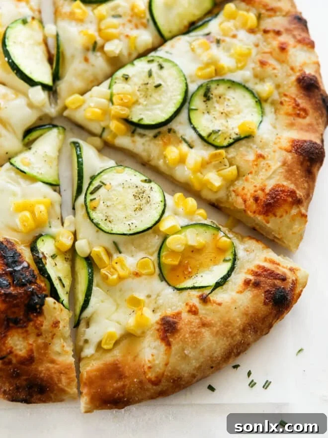 Close up of a freshly baked zucchini corn pizza with a glistening drizzle of hot honey