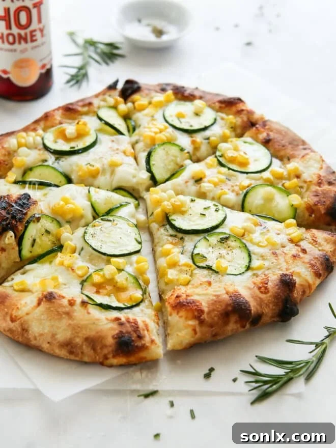 Freshly sliced zucchini corn pizza resting on a wooden board with a bottle of hot honey in the soft background