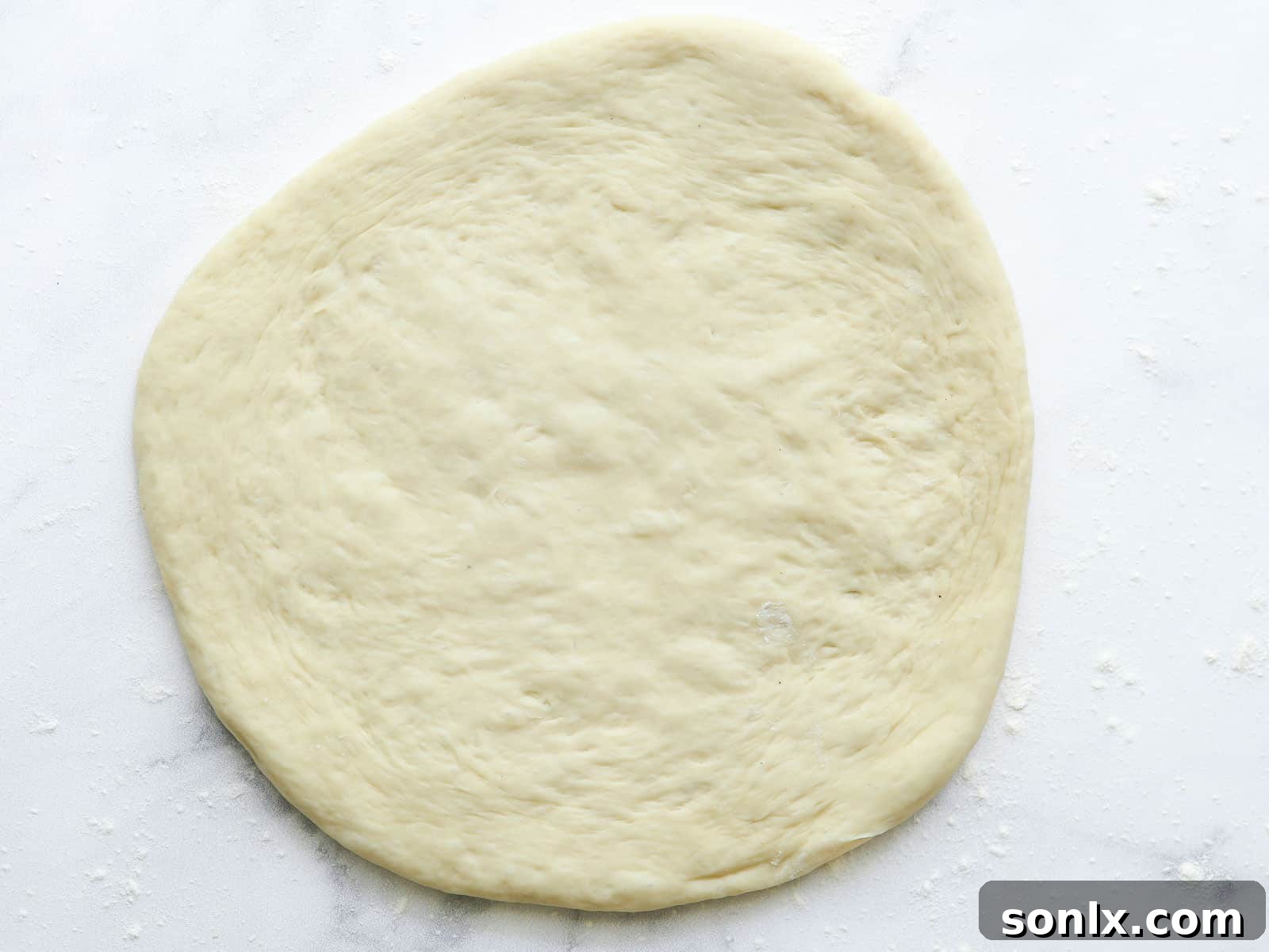 Rolled out pizza dough ready for toppings on a lightly floured kitchen counter