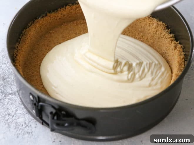 Chef pouring creamy cheesecake filling into a graham cracker crust set in a springform pan, preparing for a water bath bake.