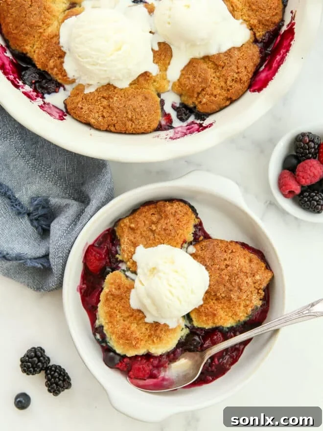 A serving of warm berry cobbler in a dish, topped with a scoop of melting vanilla ice cream, highlighting the rich fruit filling and golden biscuit topping.