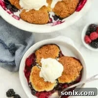 A scoop of berry cobbler in a bowl with vanilla ice cream, showing the vibrant fruit and tender topping.