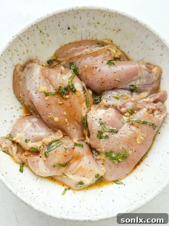 Boneless, skinless chicken thighs soaking in a vibrant easy marinade in a glass bowl, ready for grilling