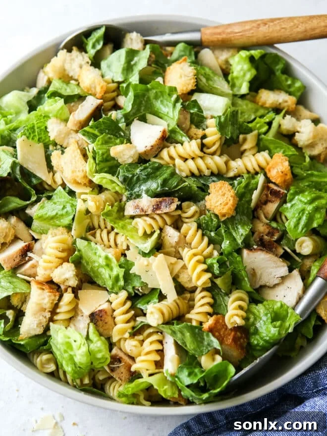 Close-up of a chicken caesar pasta salad in a bowl, featuring grilled chicken, penne pasta, crisp lettuce, and a creamy dressing