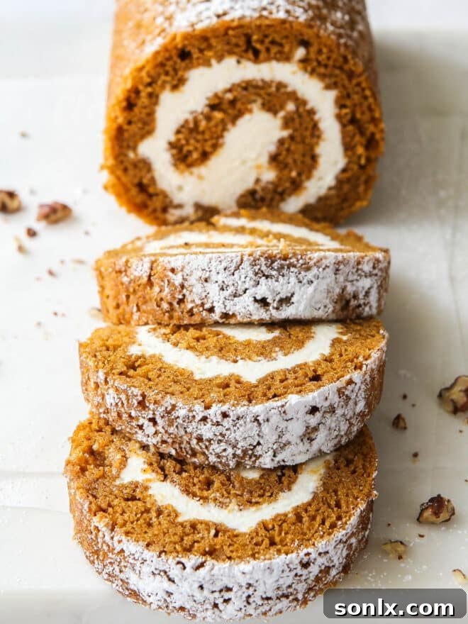Sliced pumpkin roll showcasing the beautiful spiral and creamy filling, garnished with candied pecans.