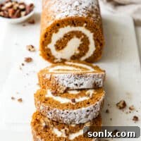 Pumpkin swiss roll cake with candied pecans on a serving plate.