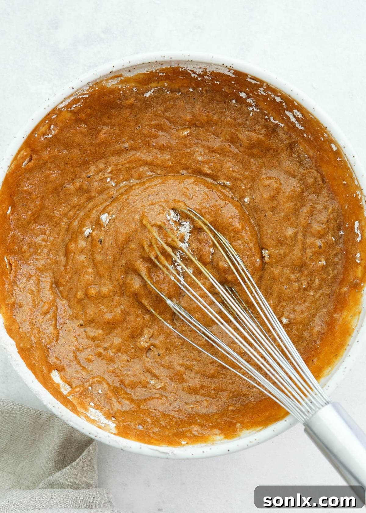 Mixing pumpkin roll cake batter in a bowl, showing the smooth, orange-hued batter.