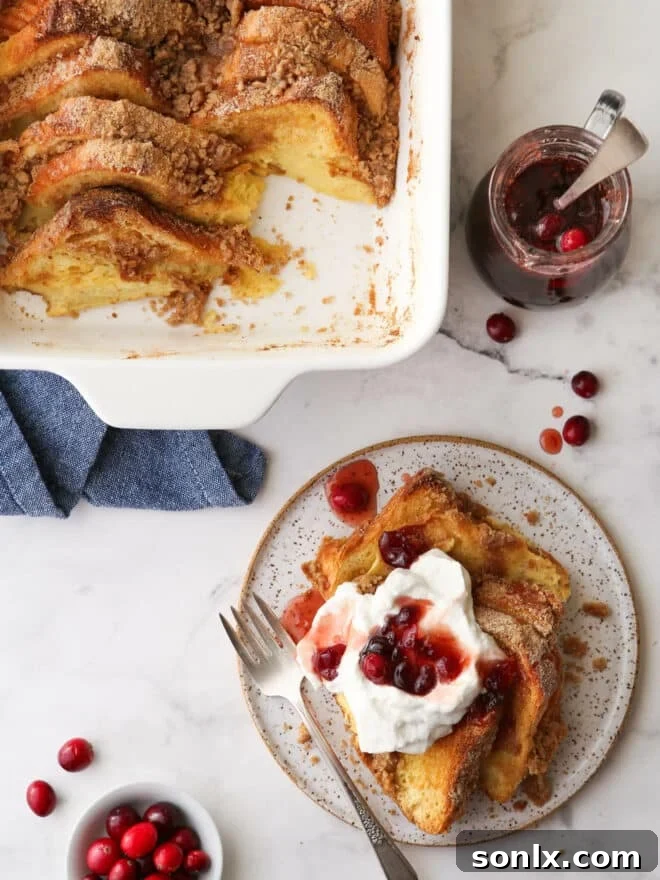 Baked French toast on a plate with whipped cream and cranberry maple syrup, ready to be enjoyed during a holiday brunch.
