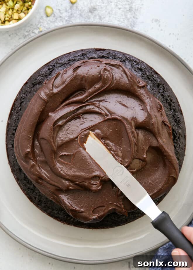 Spreading smooth chocolate ganache over a freshly baked chocolate olive oil cake
