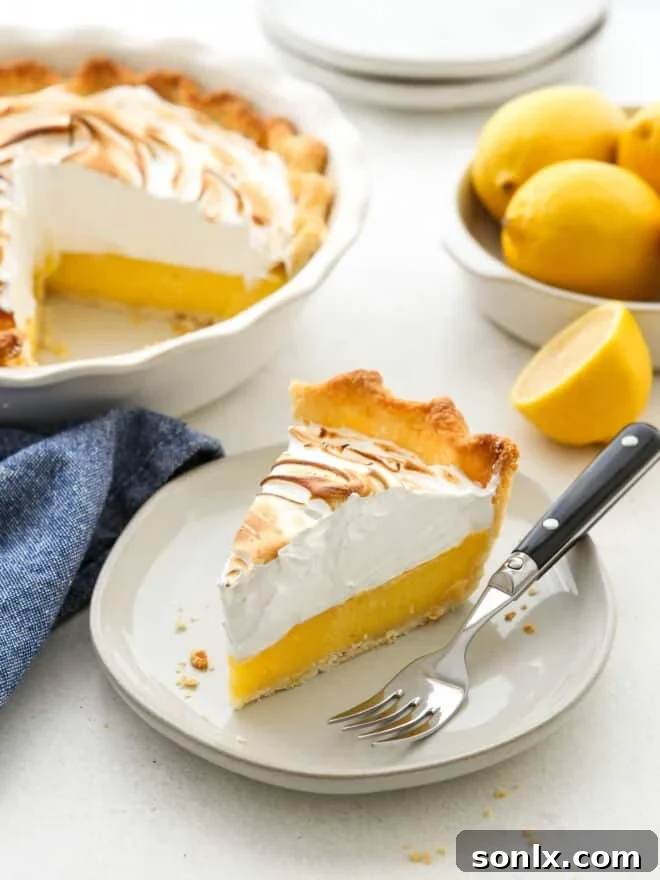 A perfectly sliced piece of lemon meringue pie on a white plate, showcasing its flaky crust, bright yellow filling, and tall toasted meringue.